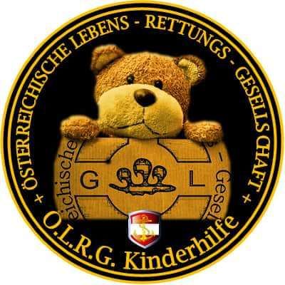 Ein kreisförmiges Logo mit einem Teddybären, der eine goldene Box mit dem Emblem des Österreichischen Kinderrettungsdienstes hält, umgeben von einem schwarzen Rand und einem goldenen Umriss.