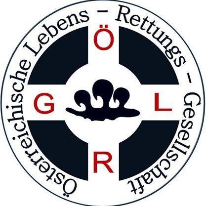 Ein kreisförmiges Emblem mit Kreuzdesign, das die Buchstaben 'G', 'R' und 'L' in Rot, Weiß und Schwarz zeigt. Das Emblem hat eine Wassermarke in der Mitte und den Text 'Lebensschutz' auf Deutsch am Rand.