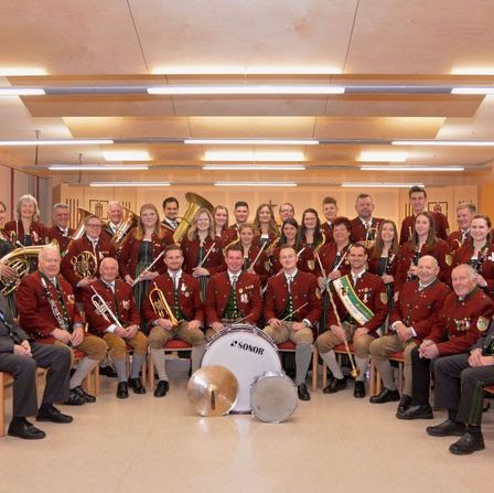 Eine Gruppe von Menschen in passenden roten und goldenen Uniformen posiert mit Musikinstrumenten für ein Foto.