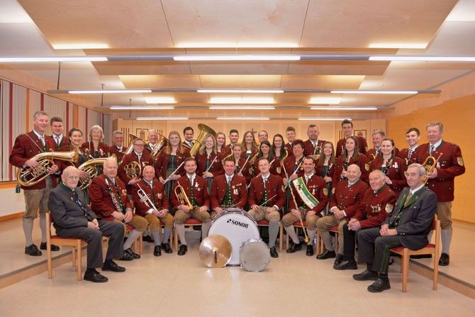 Eine Gruppe von Menschen in passenden roten und goldenen Uniformen posiert mit Musikinstrumenten für ein Foto.