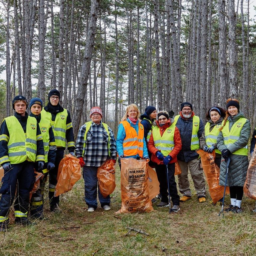 Eine Gruppe von Menschen in Reflektorwesten und Handschuhen steht in einem Wald und hält Säcke mit gesammeltem Abfall.