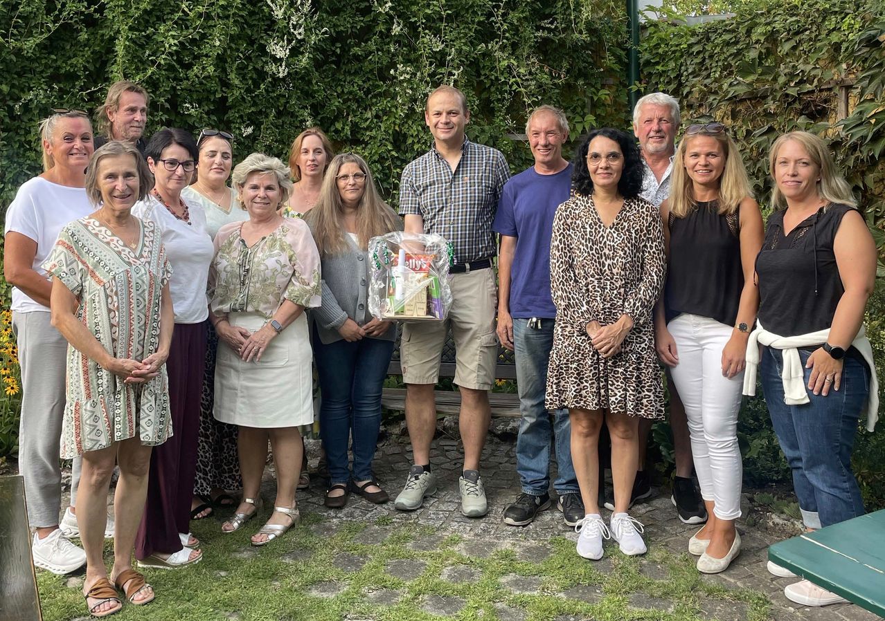 Eine Gruppe Erwachsener steht in einem Garten und lächelt für ein Foto. Ein Mann hält eine Tüte Snacks.