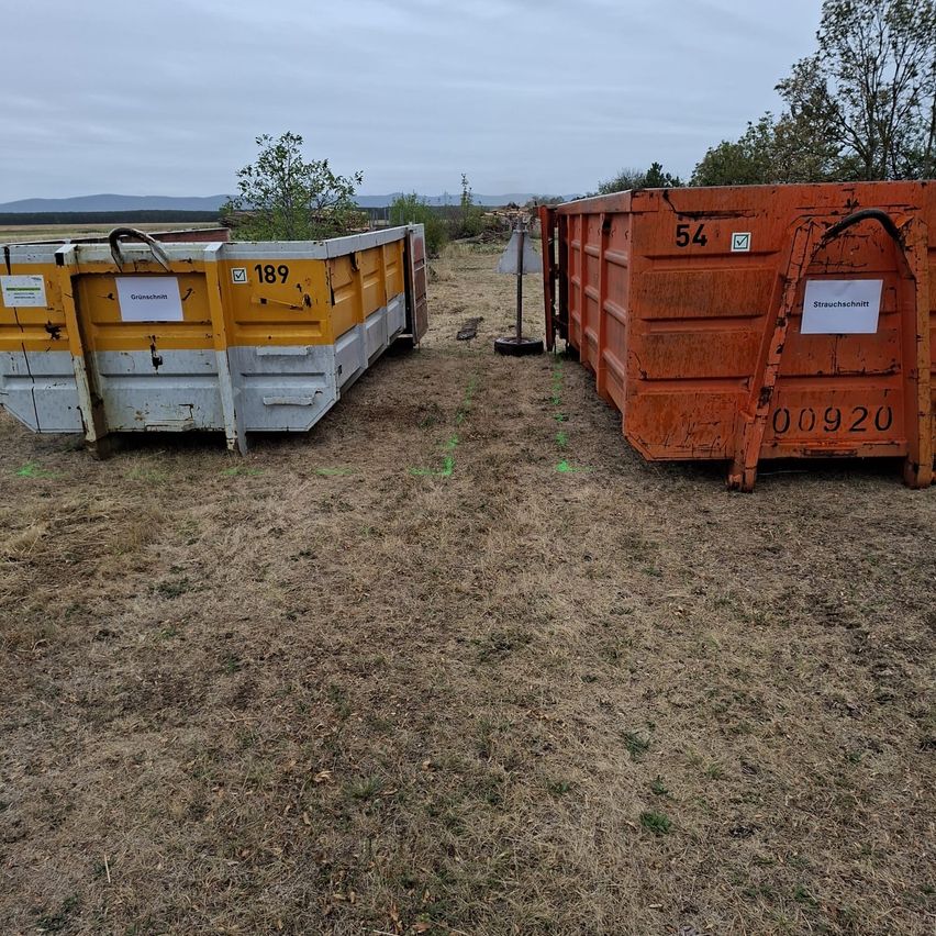 Zwei Müllcontainer stehen auf einem kahlen Feld. Einer ist gelb mit der Nummer 189 und der andere ist orange mit der Nummer 54. Beide haben Schilder, die auf Strohentsorgung hinweisen.