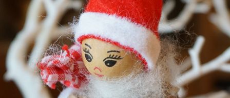 Ein kleiner Weihnachtszwerg aus Tannenzapfen steht vor weißem Hintergrund. Er trägt einen roten Hut und ein weiß-rotes Halstuch.