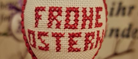 Ein Nahaufnahme eines weiß-rot bestickten Eis mit dem Wort 'FROHE OSTERN' in rotem Faden geschrieben.