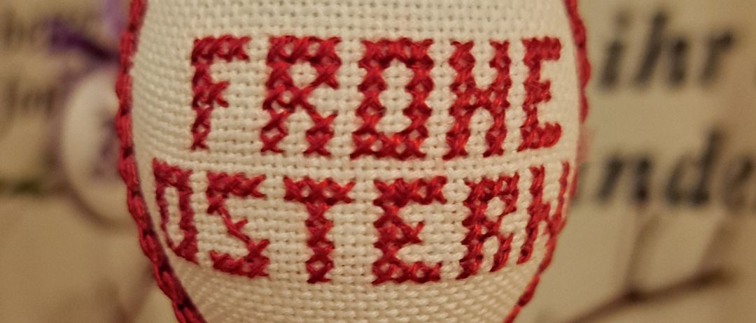 Ein Nahaufnahme eines weiß-rot bestickten Eis mit dem Wort 'FROHE OSTERN' in rotem Faden geschrieben.