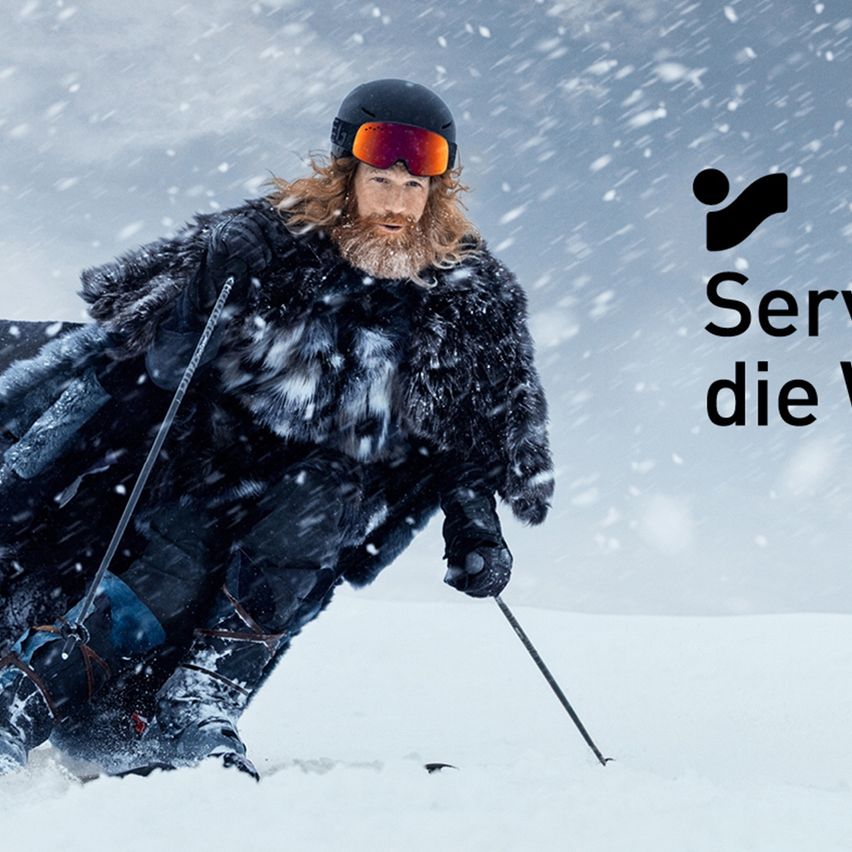 Ein Skifahrer mit Schutzbrille und Pelzmantel skisrt im Schnee. Ein Logo und der Schriftzug 'Server die W' befinden sich in der oberen rechten Ecke.
