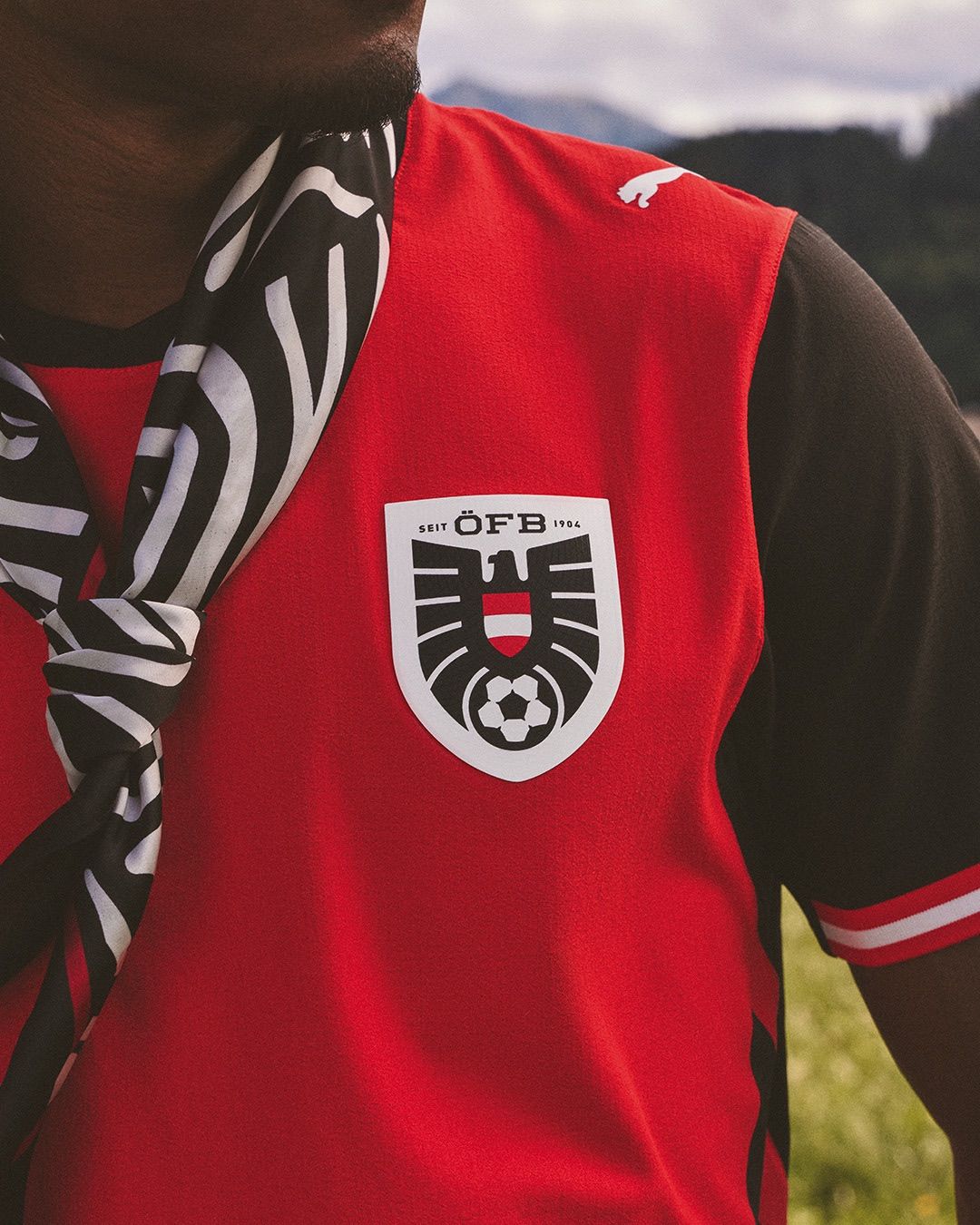Ein rotes Fußballtrikot mit weißem Emblem und schwarz-weißem Schal. Das Emblem zeigt einen Fußball und die Buchstaben OFB.