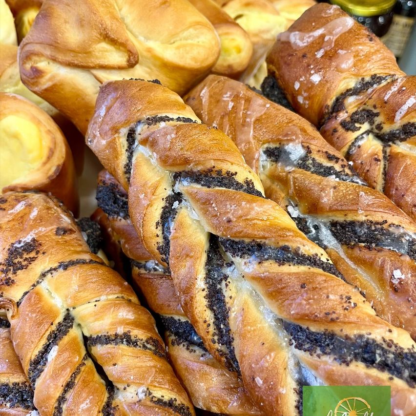 Nahaufnahme verschiedener Brotsorten, darunter geflochtene Laibe mit Mohn, auf einem Tisch.