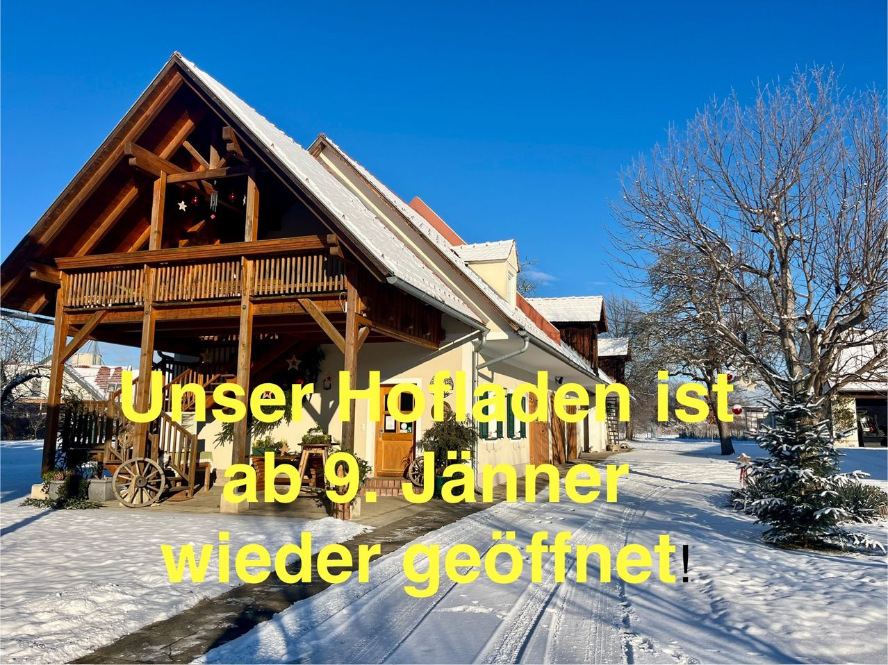 Ein Holzhaus mit einem geneigten Dach und Schnee darauf. Ein Holzrad und ein Topf stehen davor. Der Text lautet: 'Unser Hofladen ist ab 9. Januar wieder geöffnet.' Es gibt einen schneebedeckten Weg und Bäume in der Umgebung.