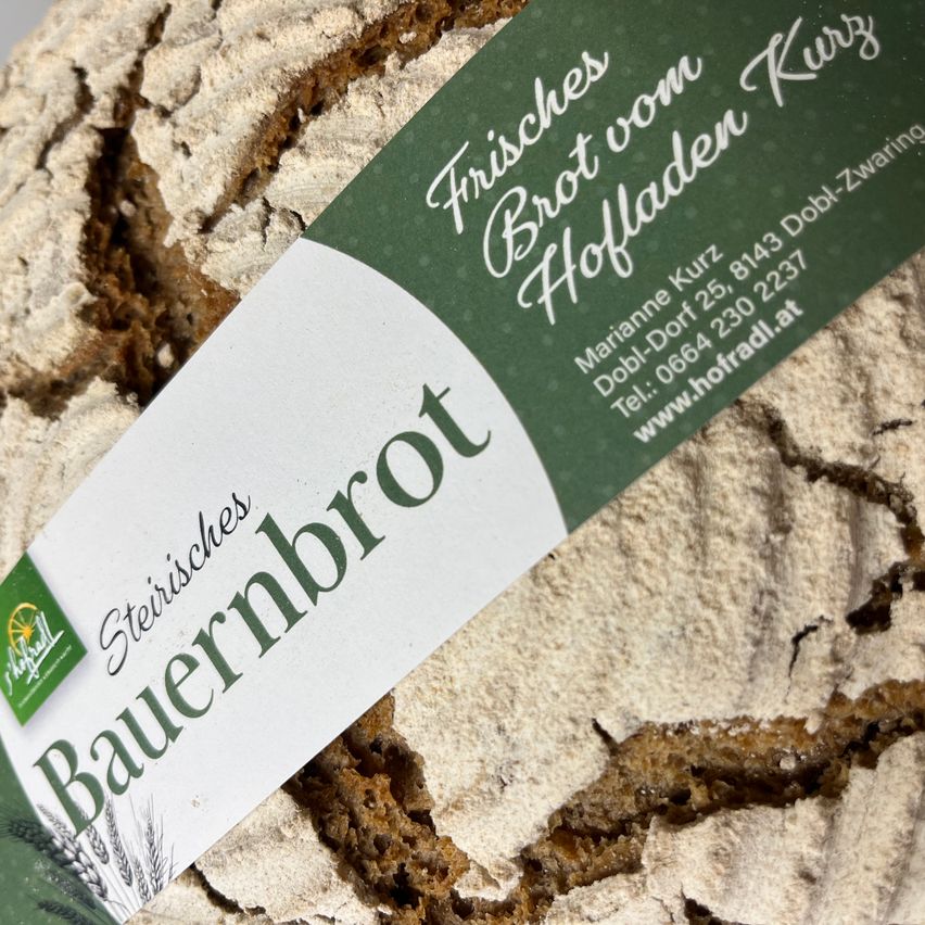 A slice of Styrian farmer's bread with a label reading 'Fresh Bread from Holleden Kurz'. The label includes contact details for Marianne Kurz.