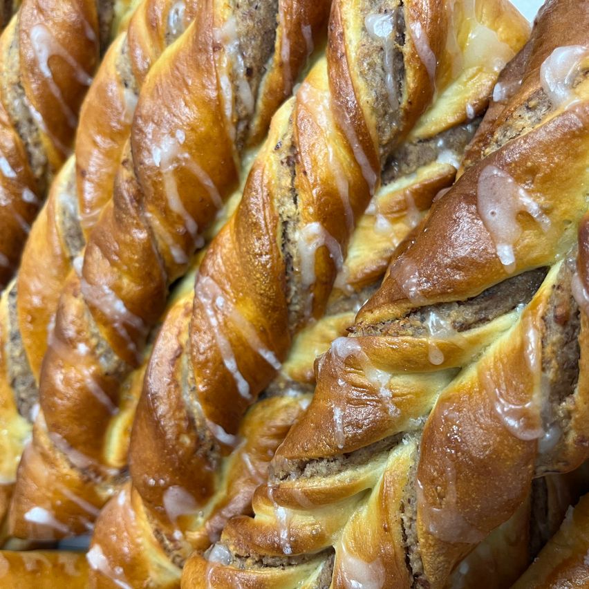 A close-up of twisted pastries with a filling and white icing on top. The pastries have a golden-brown crust.