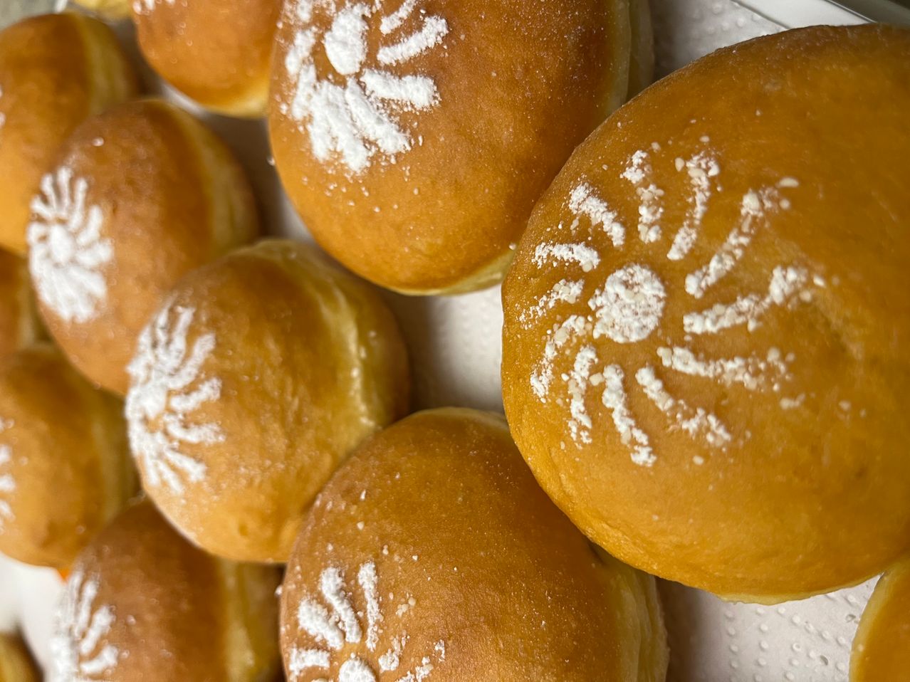 A close-up view of several golden brown donuts, dusted with powdered sugar and featuring intricate designs on their tops.