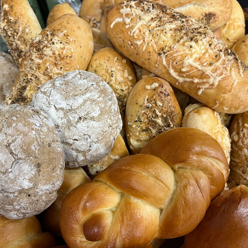 Eine Nahaufnahme verschiedener Brotsorten, darunter einige mit Käse und Kräutern auf der Oberseite, andere mit einer Puderzuckerschicht und wieder andere mit aufwendigen Zöpfen.