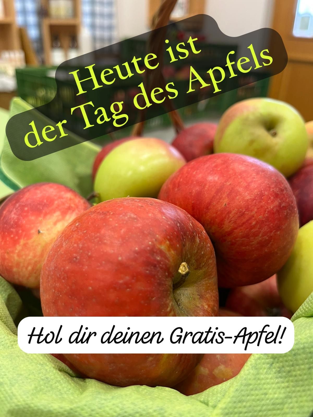 A close-up view of a basket filled with red and green apples. White text overlay reads, 'Today is the apple of the day.' In the foreground, a green leaf is visible.