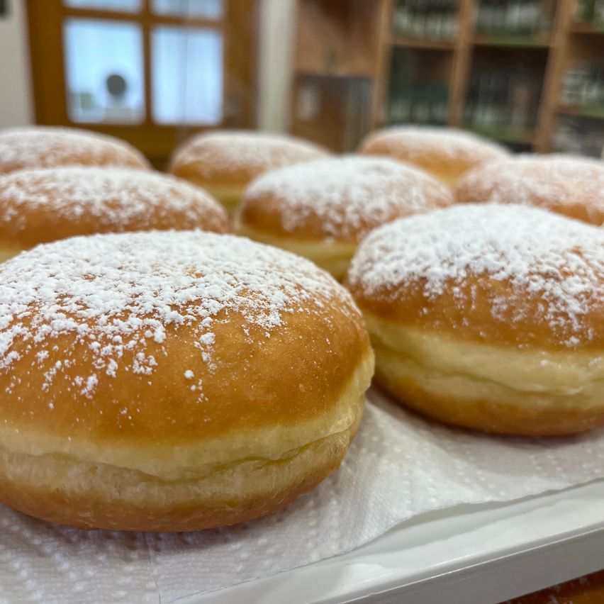 A tray of donuts dusted with powdered sugar is shown, with a wooden door and shelves in the background.
