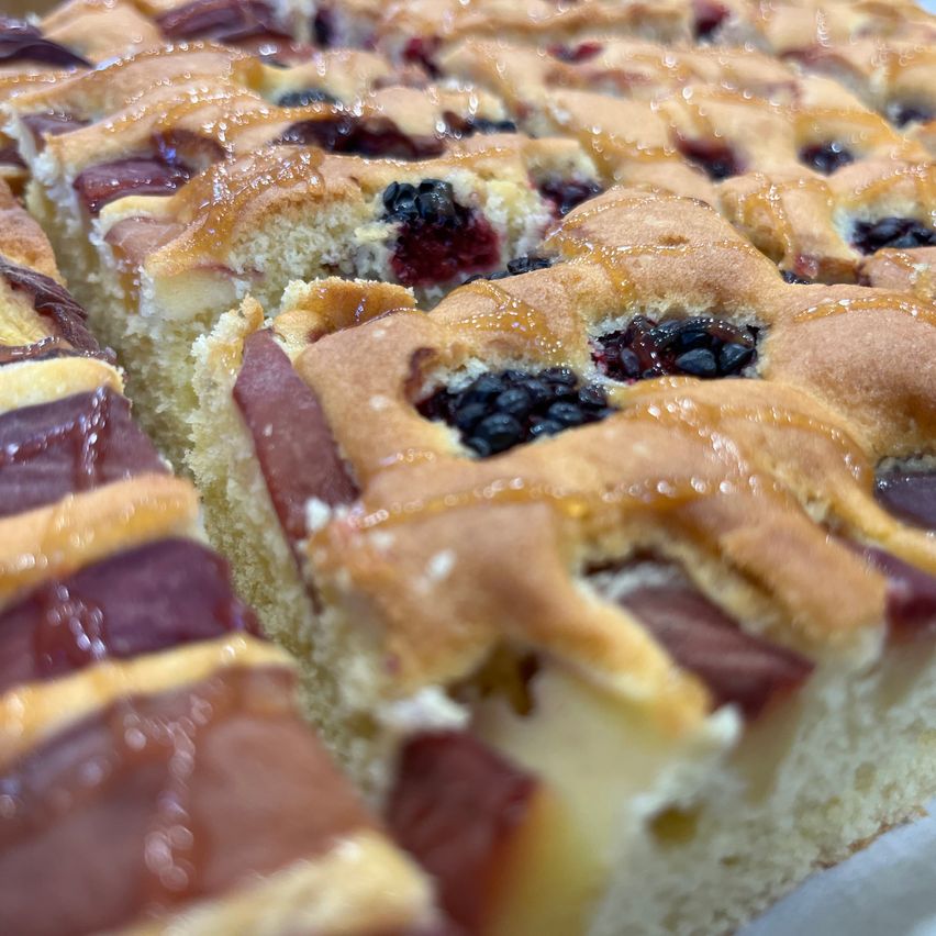 Ein Nahaufnahme eines geschnittenen Obstkuchens mit Brombeer- und Apfelfüllung, überzogen mit einem Gitterboden und mit Sirup übergossen.