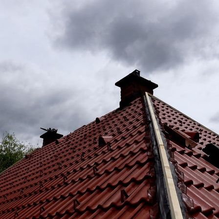 Ein Nahaufnahme eines roten Ziegeldachs mit zwei Schornsteinen unter einem bewölkten Himmel.