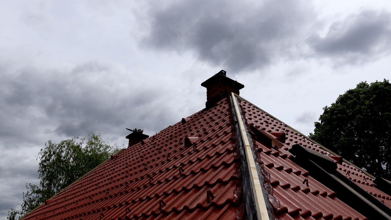 Ein Nahaufnahme eines roten Ziegeldachs mit zwei Schornsteinen unter einem bewölkten Himmel.