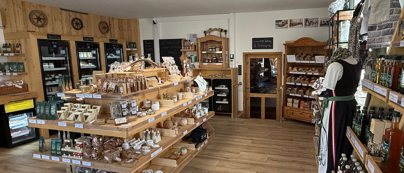 Ein Innengeschäft mit Holzregalen, die mit verschiedenen Produkten gefüllt sind. Die Regale sind ordentlich angeordnet, und der Boden ist aus Holz. Die Decke hat eine kreisförmige Beleuchtung. Es gibt auch Holzschränke und einen Spiegel an der Wand.