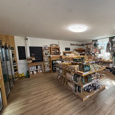 Ein Innenansicht eines Ladens mit Holzregalen gefüllt mit verschiedenen Produkten, einer Tafel mit Schrift und einer hellen Deckenleuchte.