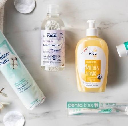 Eine Auswahl an Schönheitsprodukten auf einer Marmoroberfläche. Zu den Produkten gehören eine Flasche Mizellenwasser, eine Flasche Körperlotion, eine Tube Zahnpasta und eine Packung Wattepads.