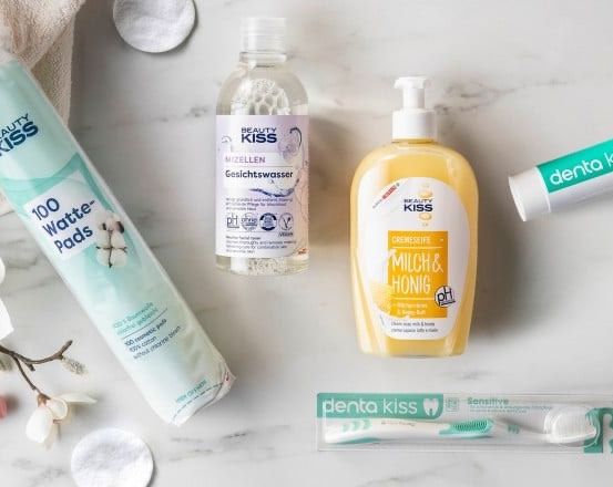 Eine Auswahl an Schönheitsprodukten auf einer Marmoroberfläche. Zu den Produkten gehören eine Flasche Mizellenwasser, eine Flasche Körperlotion, eine Tube Zahnpasta und eine Packung Wattepads.