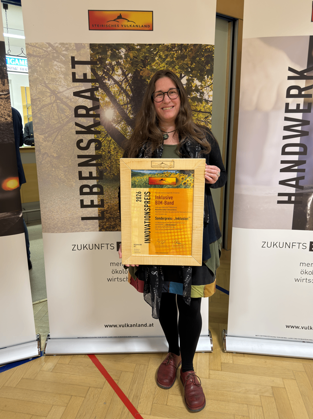 A woman holding a framed award in front of a banner that reads 'Lebenskraft' and 'Innovationspreis'.