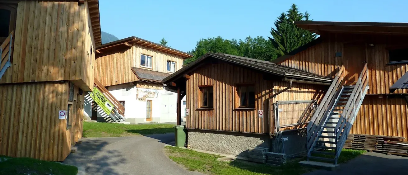 Eine Reihe von Holzhäusern mit Treppen und einer Einfahrt unter einem klaren blauen Himmel mit Bäumen im Hintergrund.