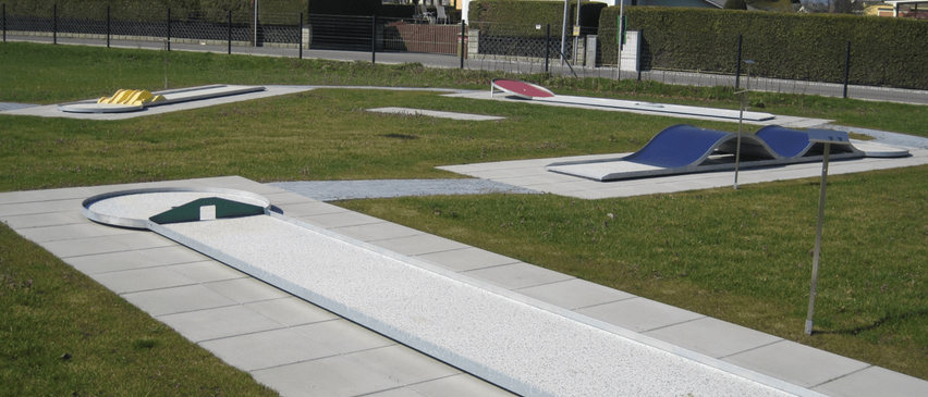 Ein Blick auf einen Golfplatz mit mehreren Löchern und Grasflächen. Im Hintergrund steht ein Haus mit einem Zaun darum.