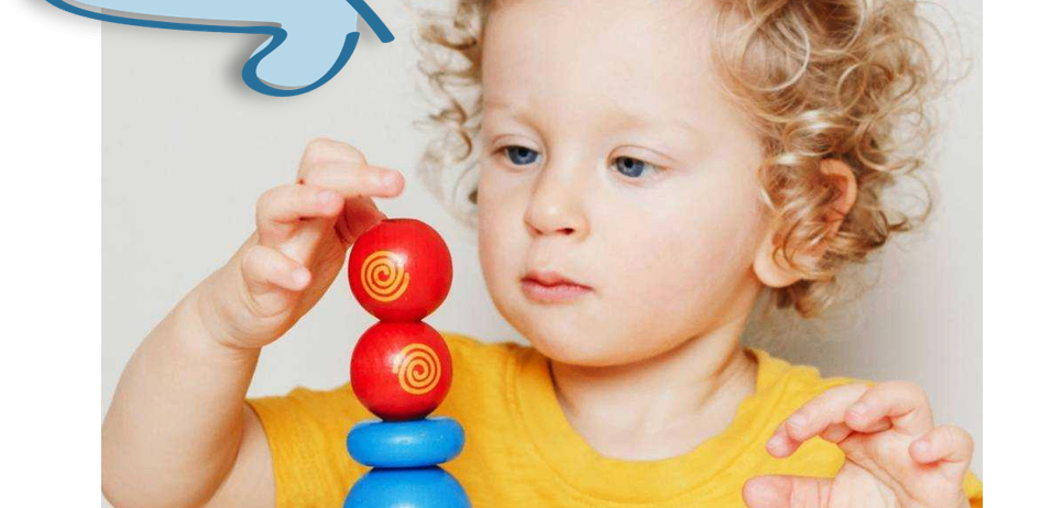 Ein kleines Kind mit lockigem Haar spielt mit einem bunten Stapel Ringe und hält einen roten Ring oben.