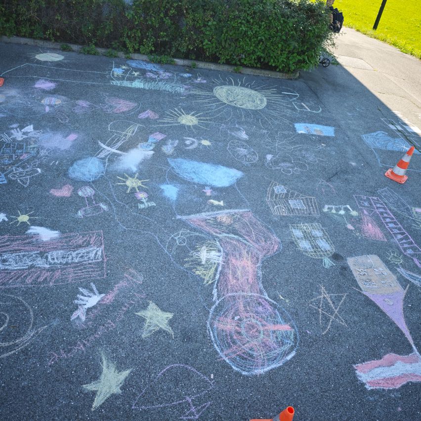 Eine Straße, die mit farbenfrohen Kreidezeichnungen bedeckt ist, darunter Sonnen, Sterne und eine Stadtlandschaft. Es gibt Verkehrskegel an der Seite.
