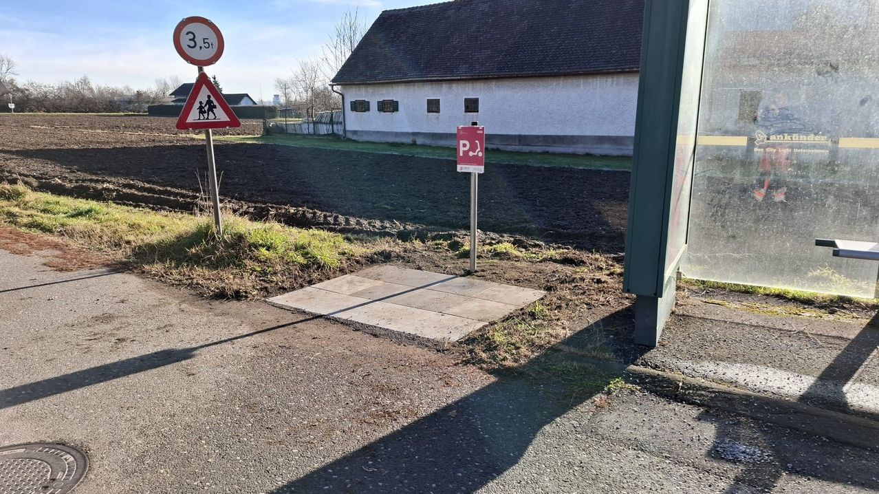 Ein gepflasterter Bereich mit einem Fußgängerübergangsschild, einem Geschwindigkeitsbegrenzungsschild und einem Gebäude im Hintergrund.