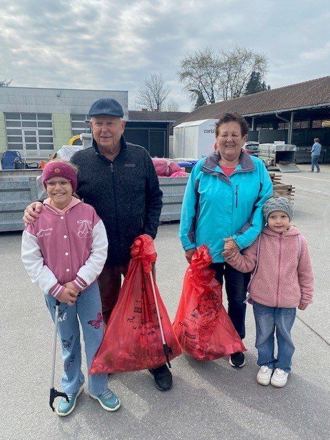 Drei Personen stehen draußen mit roten Tüten in der Hand, eine Frau in der Mitte lächelt und hält ein Kind auf jeder Seite.