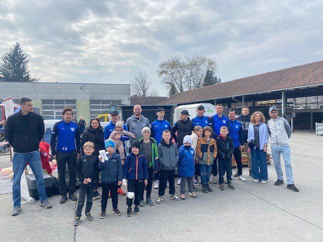 Eine Gruppe von Menschen, darunter Kinder, steht zusammen und lächelt für ein Foto vor einem Gebäude.