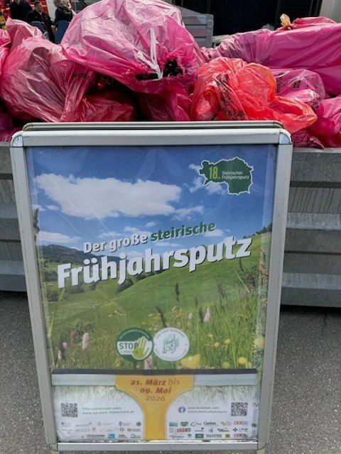 Ein Schild bewirbt die 'grobe steirische Fruhjahrsputz' Veranstaltung mit einem Feld im Hintergrund und pinken Mülltüten.