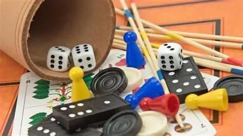 Eine Sammlung von Brettspiel-Spielsteinen, einschließlich Würfel, Spielfiguren und Spielbretter, sind auf einer orangefarbenen Oberfläche verstreut. Die Würfel befinden sich in einem zylindrischen Behälter.
