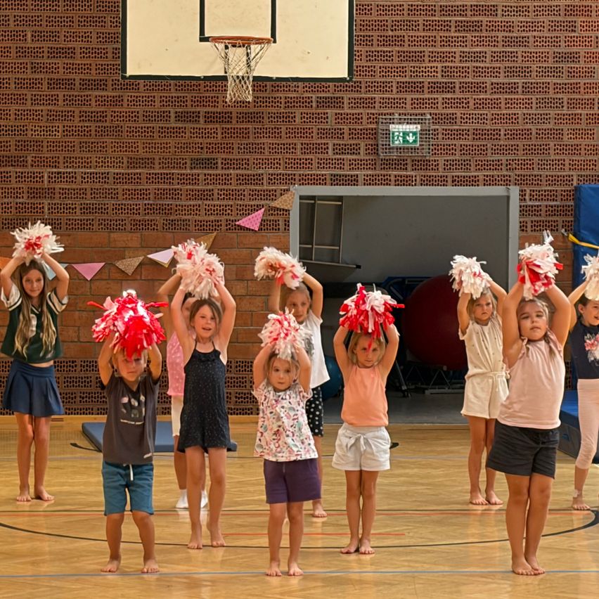 Eine Gruppe junger Mädchen in einer Turnhalle, die rote und weiße Pompons halten und eine Cheerleader-Routine üben.