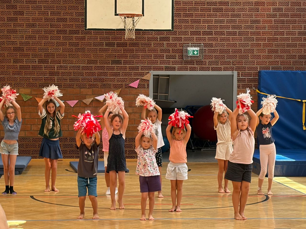 Eine Gruppe junger Mädchen in einer Turnhalle, die rote und weiße Pompons halten und eine Cheerleader-Routine üben.