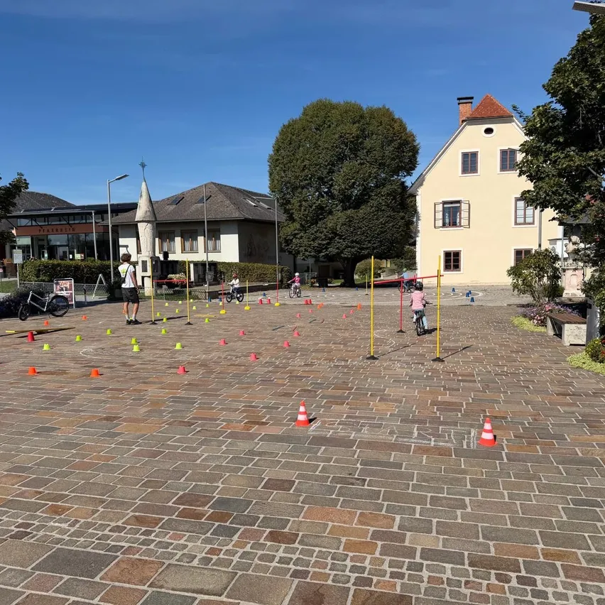Eine Gruppe von Menschen spielt ein Spiel auf einer Kopfsteinpflasterstraße. Mehrere orangefarbene und gelbe Kegel markieren das Spielfeld.