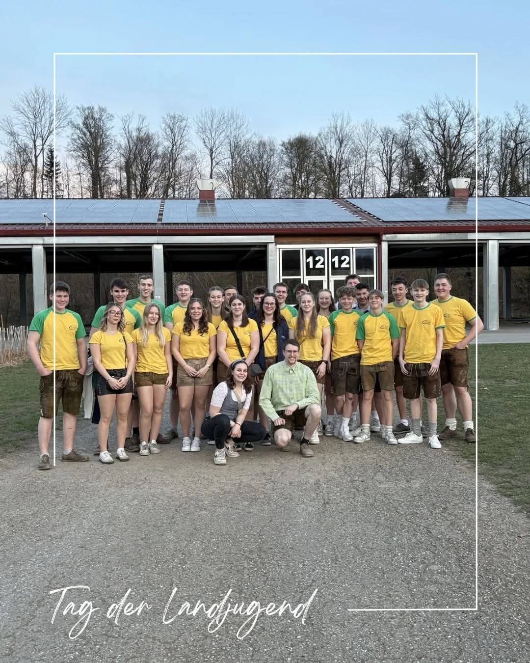 Eine Gruppe von Menschen in passenden gelben und grünen Shirts und Shorts steht vor einem Gebäude mit Solarpanelen. Sie lächeln für ein Foto.