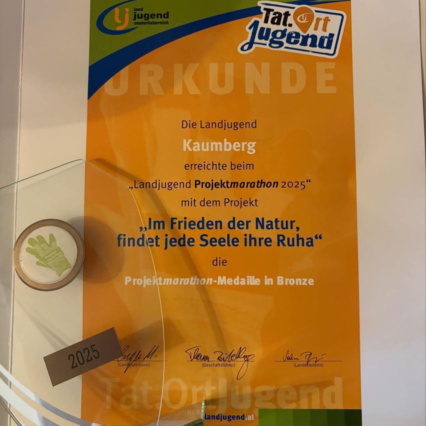 Ein Zertifikat für den Jugendprojektmarathon 2025 ist an einer Wand ausgestellt. Es ist bronzefarben und hat eine Botschaft über das Finden von Frieden in der Natur.