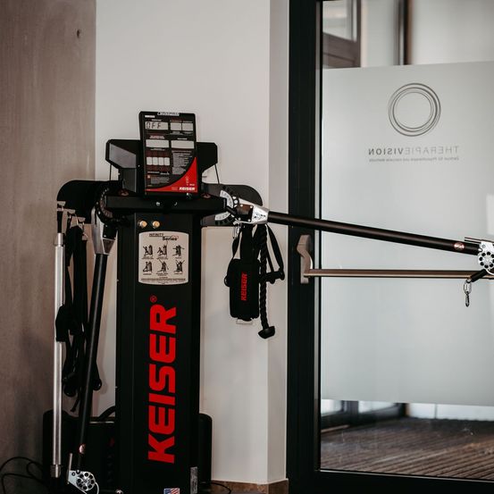 Ein schwarzer und roter Fitnesstrainer namens Keiser befindet sich in einem Raum mit einer Glastür und einem Logo.