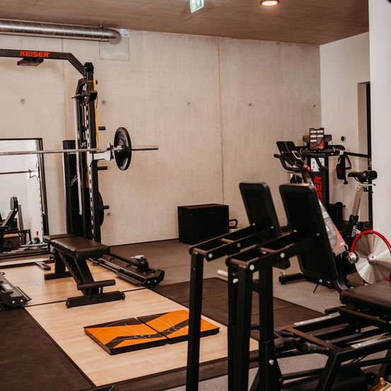 Ein Fitnessstudio mit einem Gewichtsständer, einer Bank und verschiedenen Trainingsgeräten. Es gibt ein rotes Fahrrad und einen Spiegel an der Wand.