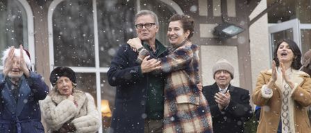 Ein Mann und eine Frau umarmen sich lächelnd während einer schneereichen Veranstaltung. Sie sind von anderen Menschen umgeben.