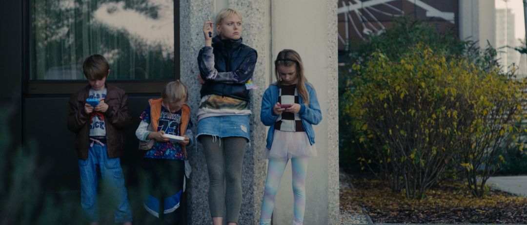 Eine Frau und drei Kinder stehen draußen und schauen auf ihre Telefone. Die Frau hält ein Telefon in der linken Hand, während die Kinder auf ihre schauen.