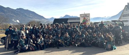 Eine Gruppe von Menschen in Kostümen mit Instrumenten posiert für ein Foto vor Bergen und einem Banner mit einem Comic-Charakter.