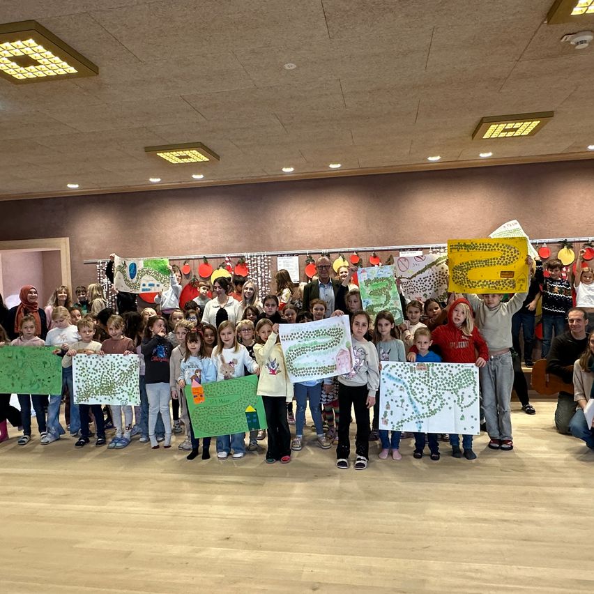 Eine Gruppe von Kindern in einer Halle, die Schilder halten, posiert für ein Foto. Ein Erwachsener steht unter ihnen.