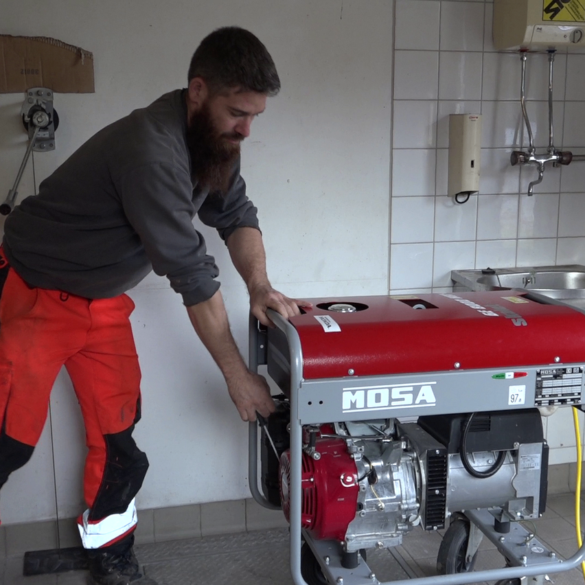 Ein bärtiger Mann justiert einen roten MOSA-Generator mit Rädern in einer Garage.