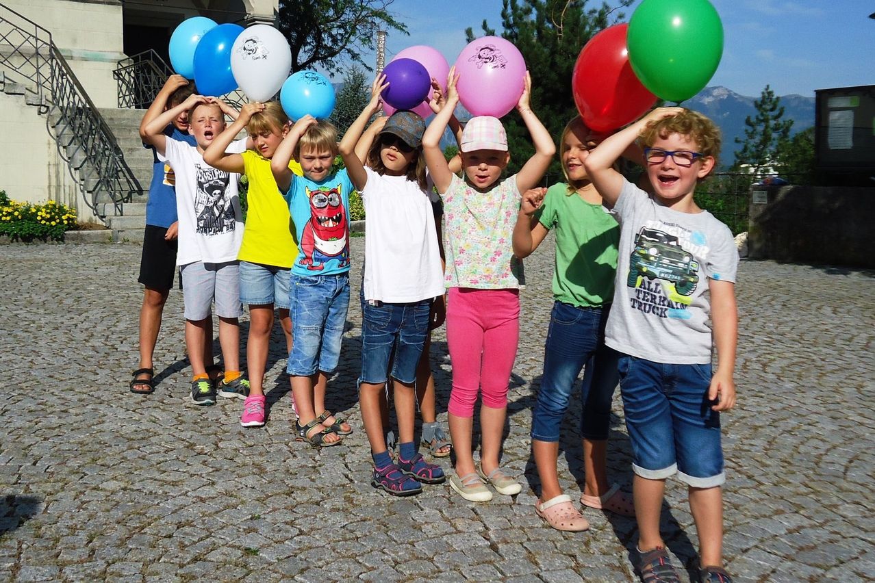 Eine Gruppe von Kindern, die Luftballons halten, steht auf einer Kopfsteinpflasterstraße. Sie scheinen eine Menge Spaß zu haben.